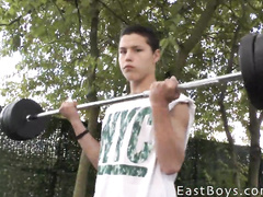 Cute and tender gay guy is lifting weights outdoors